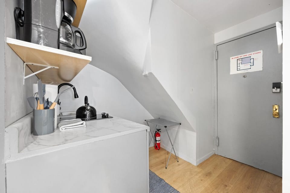 Another angle of the kitchen with a grey door, white cabinets, and a fire extinguisher on a foldable stand.