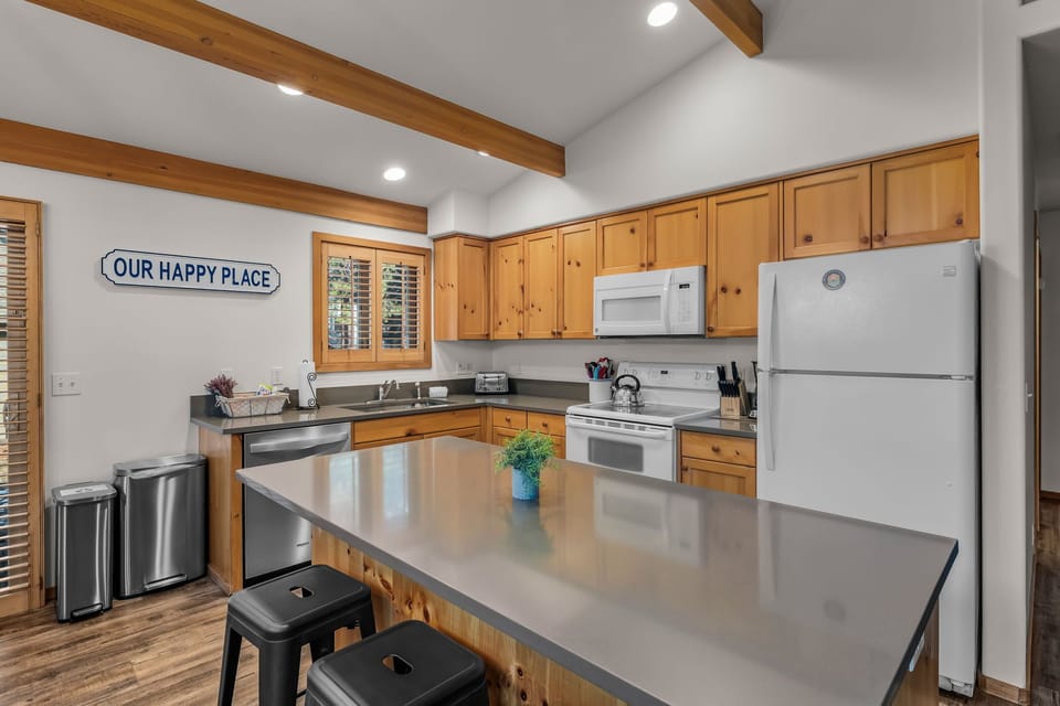 Cook your favorite meals in this fully-equipped kitchen with warm wood cabinets, modern appliances, and cheerful 'Our Happy Place' charm.