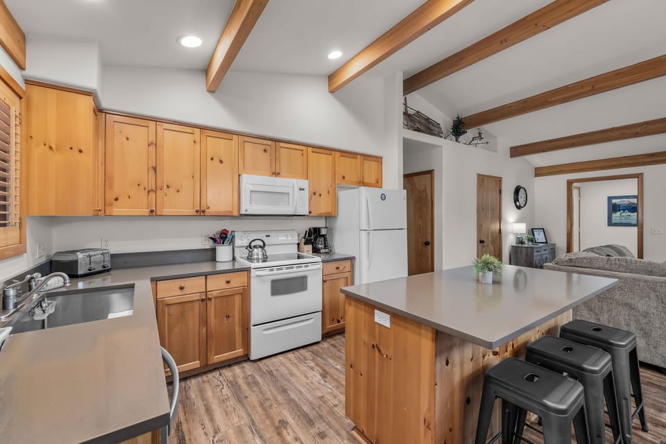 Your fully-equipped kitchen features warm wood cabinets and exposed beams, creating the perfect space for preparing meals together during your mountain getaway.