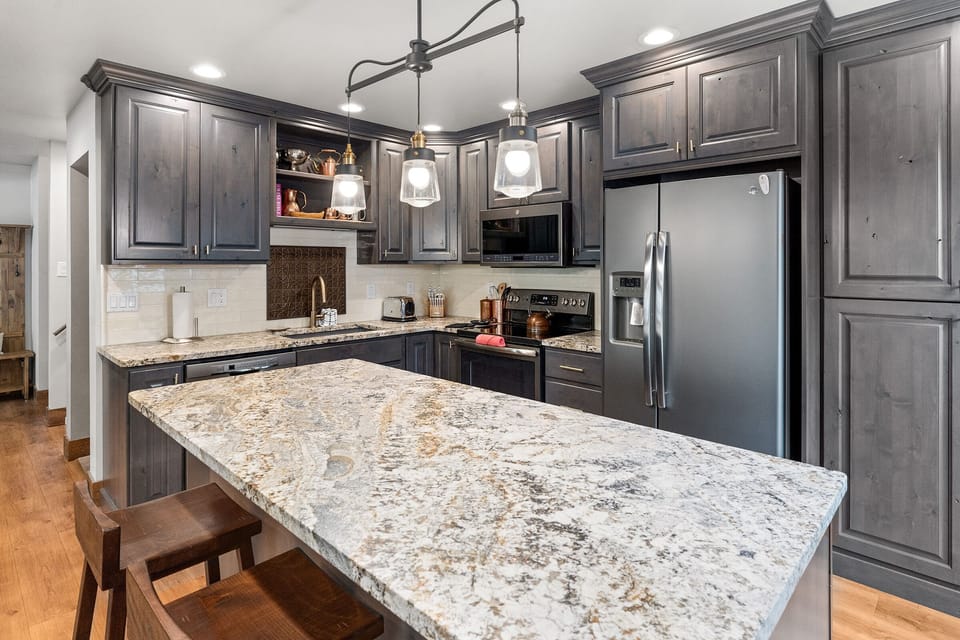 Large kitchen island, grey cabinets, brown stools.