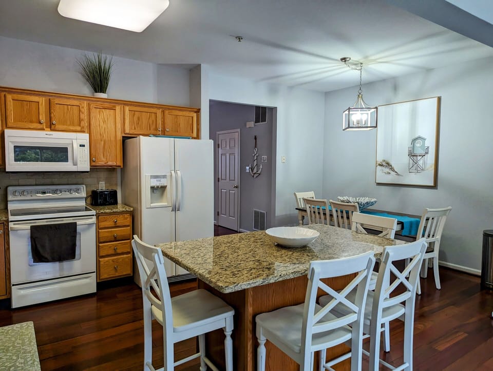 38157 Greenport Lane, South Hampton - gourmet kitchen - Modern kitchen featuring warm oak cabinetry, granite countertops, and a central island with breakfast bar seating. The open-concept layout flows seamlessly into the bright dining area.