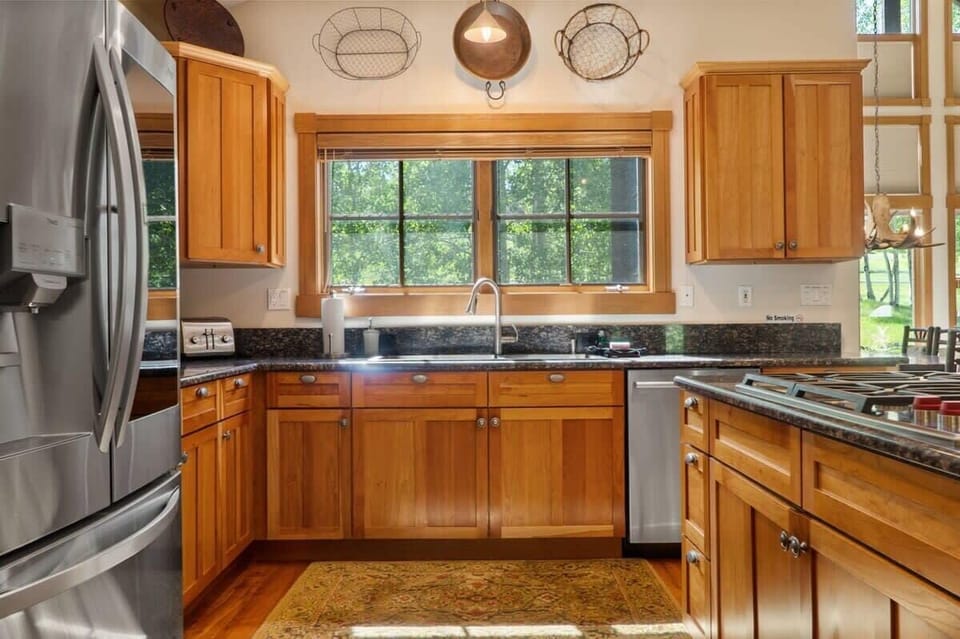 The fully equipped kitchen features high-end appliances, a large kitchen island with three barstools, ample cabinet and counter space, and classic wood finishes.