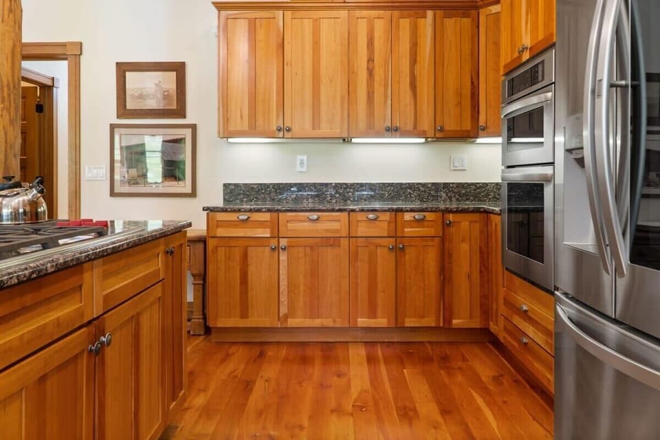 The fully equipped kitchen features high-end appliances, a large kitchen island with three barstools, ample cabinet and counter space, and classic wood finishes.