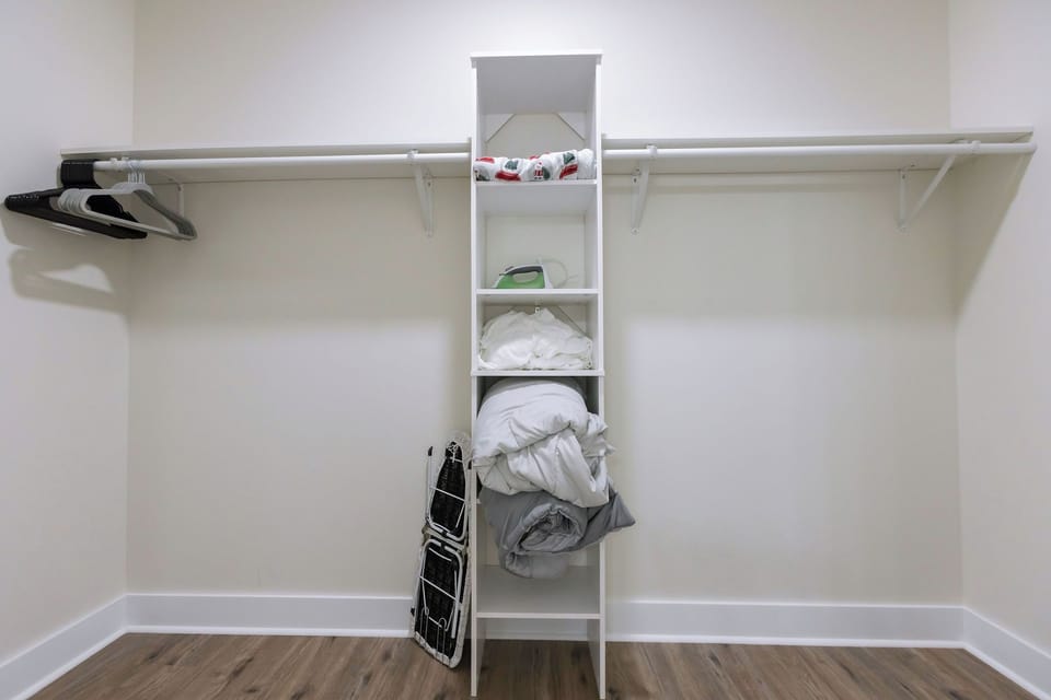 The master closet with an iron, ironing board, hangers, and extra blankets 