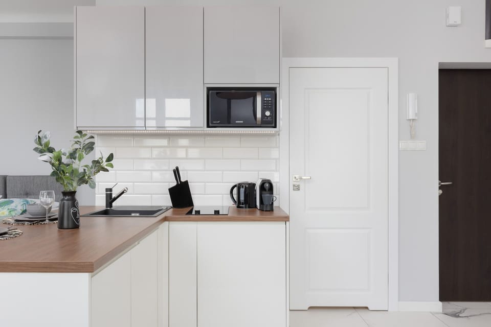 A compact and elegant kitchen in white tones is equipped with sleek modern appliances and minimalistic decor for a clean, functional look.