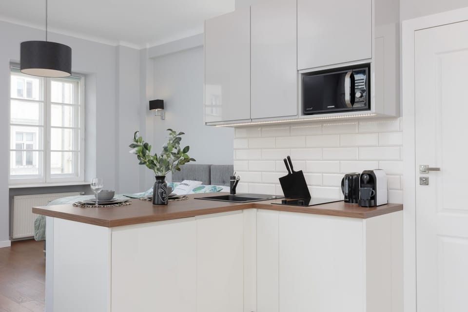 A compact and elegant kitchen in white tones is equipped with sleek modern appliances and minimalistic decor for a clean, functional look.