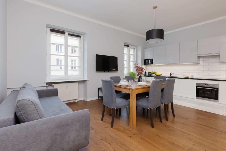 A spacious and bright living area featuring a gray sofa, wooden floors, and modern decor, creating a cozy and inviting atmosphere.