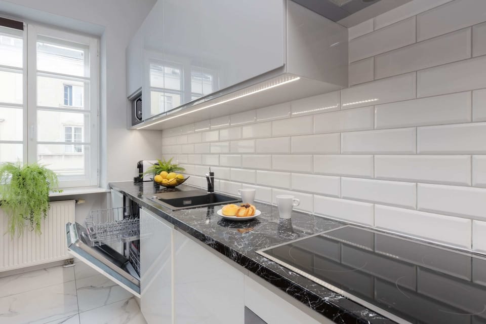 A fully equipped, modern kitchen with white cabinetry, a dark countertop, and a stylish subway tile backsplash.