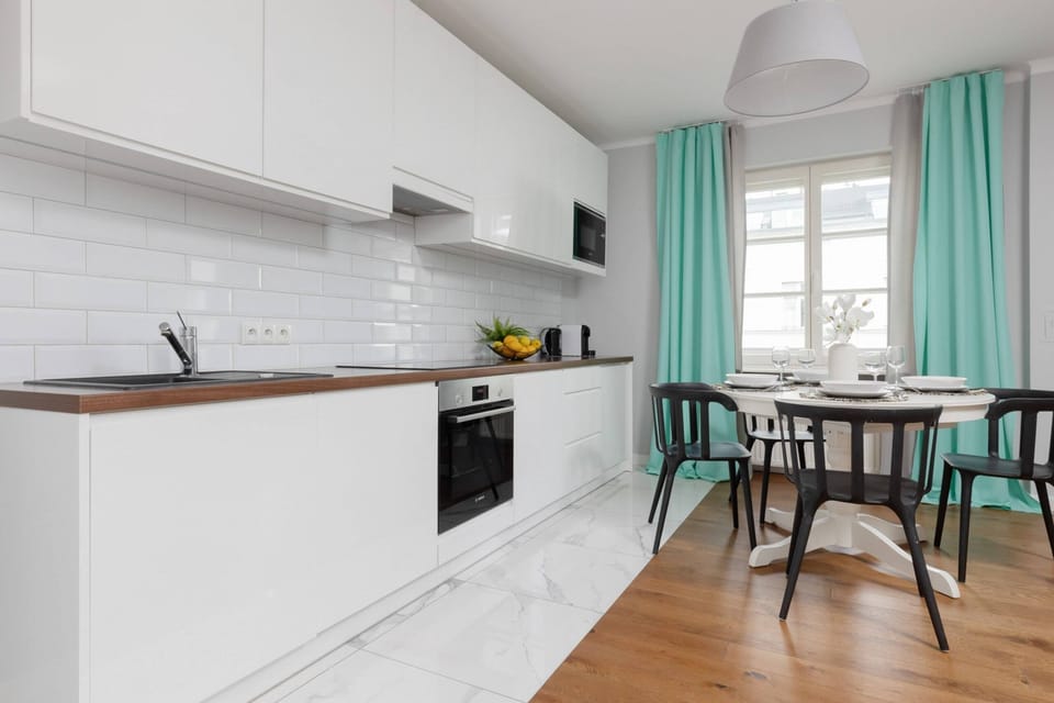 A modern open-plan kitchen with white cabinetry, a wooden countertop, and a dining area with turquoise curtains adding vibrancy to the space.