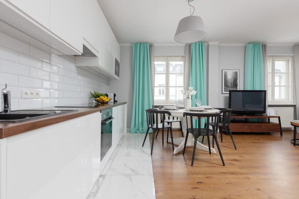 A modern open-plan kitchen with white cabinetry, a wooden countertop, and a dining area with turquoise curtains adding vibrancy to the space.