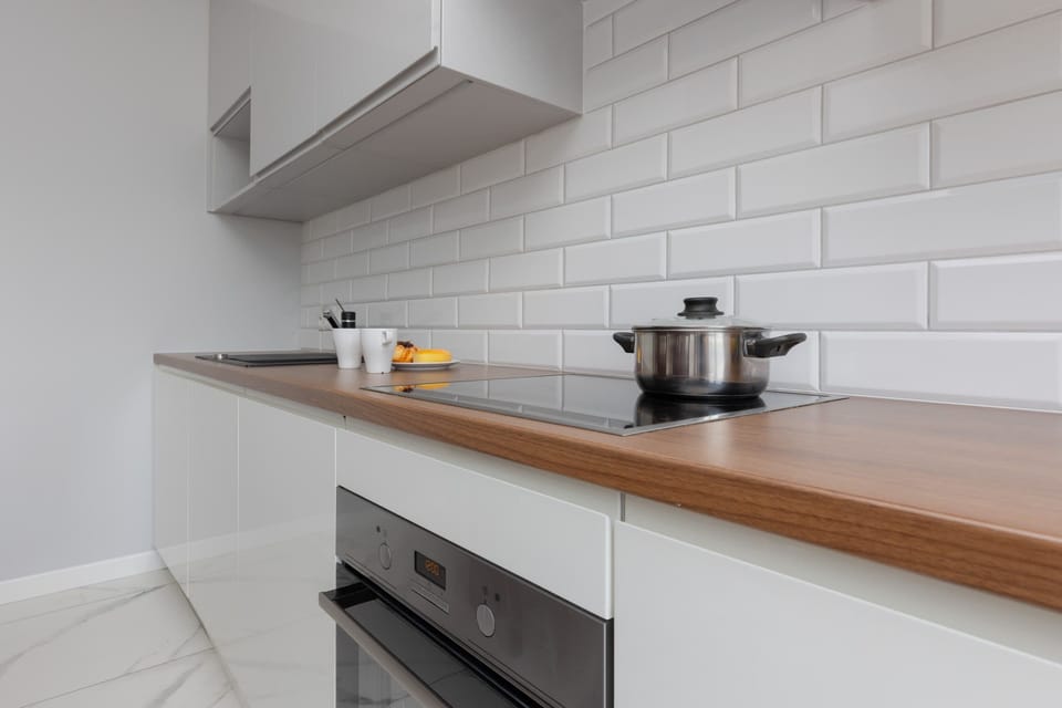 A modern, well-equipped kitchen with white cabinetry, a sleek subway tile backsplash, and wooden countertops.