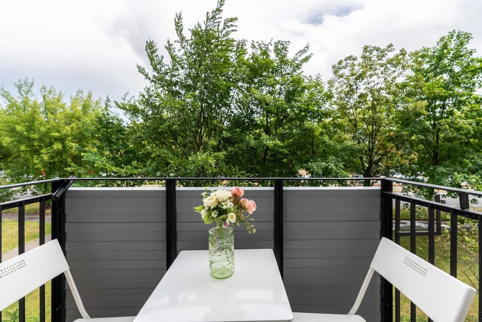 A charming balcony with a table and chairs, surrounded by lush green trees.

