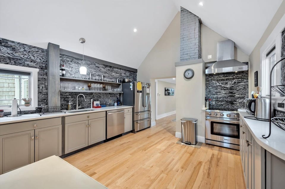 Dark stone walls, gray cabinetry, stainless steel oven with hood, hardwood floors, and a high ceiling
