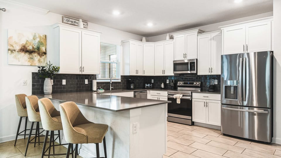 Sleek modern kitchen with stainless appliances, big island, bar seating and bright light
