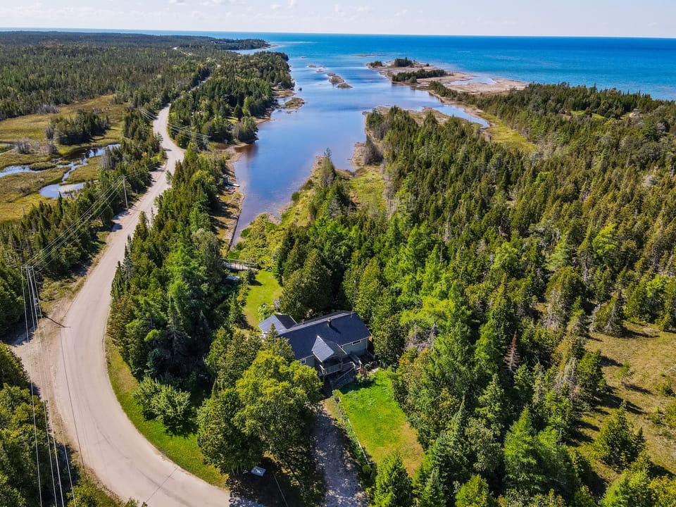An incredible aerial view showcasing the property’s stunning location, nestled amidst lush greenery and steps from the crystal-clear waters of Lake Huron, Northern Bruce Peninsula.