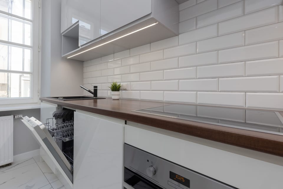 A clean and fully-equipped kitchen area featuring white cabinetry, a tiled backsplash, and wooden countertops.