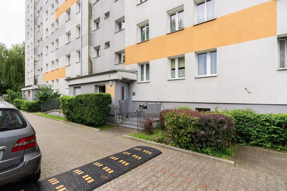 The exterior of the building, showcasing parking spaces and a landscaped area for residents.
