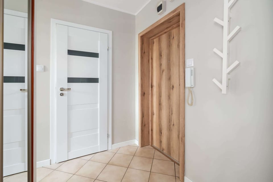 A bright hallway with tiled flooring, wooden doors, and wall hooks for added functionality.
