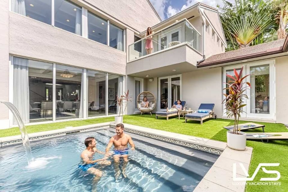 Outdoor Heated Pool with Waterfall feature, separate Hot Tub, Cabana, BBQ and Lounge Chairs all covered in artificial turf. 