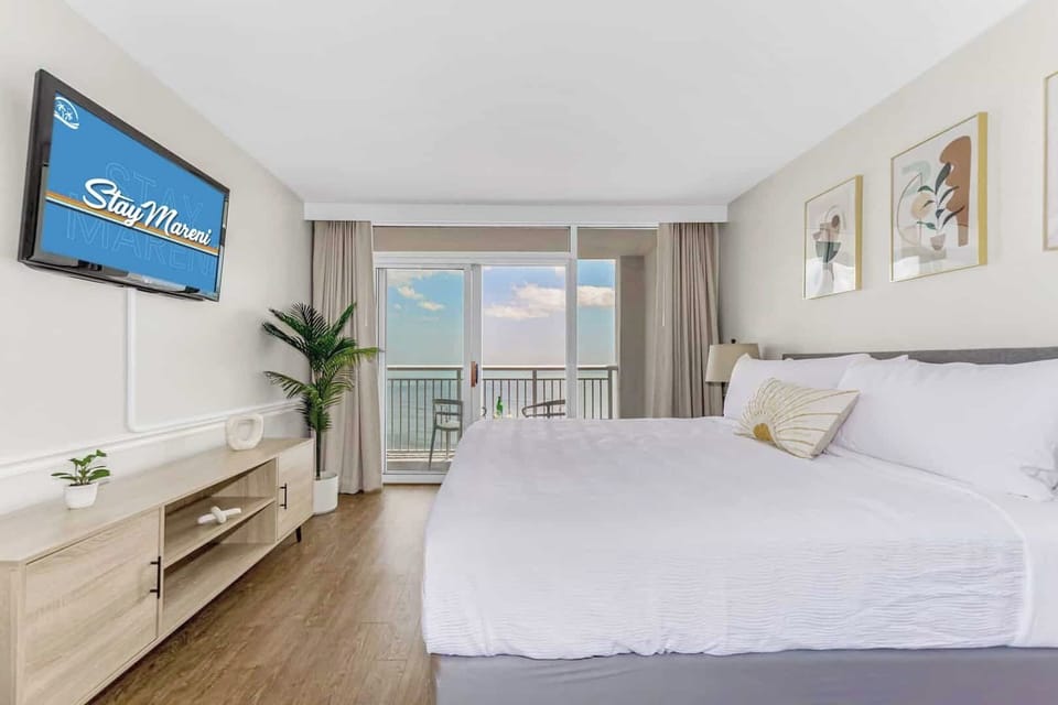 Wake up to breathtaking ocean views in this modern, serene bedroom featuring a plush king-size bed, stylish decor, and direct access to a private balcony. Relax in comfort with a flat-screen TV and soothing natural tones of the waves from the ocean.