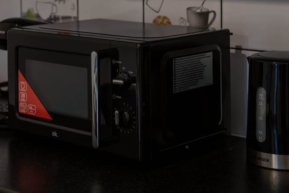 A close-up of a microwave and coffee setup on a sleek black kitchen counter.

