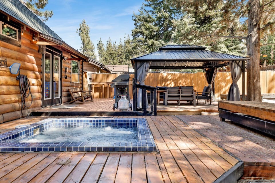 Spacious backyard with a relaxing hot tub, BBQ, outdoor dining area, comfy seating, and charming string lights perfect for peaceful evenings outdoors.