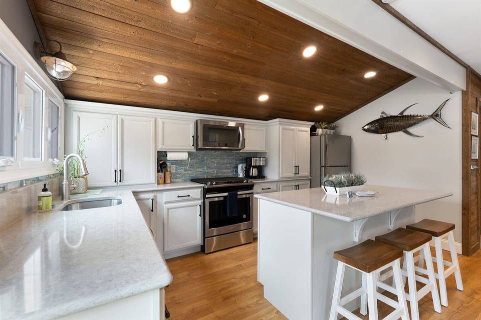 Stylish open kitchen w/ stainless appliances and wood-paneled ceiling.