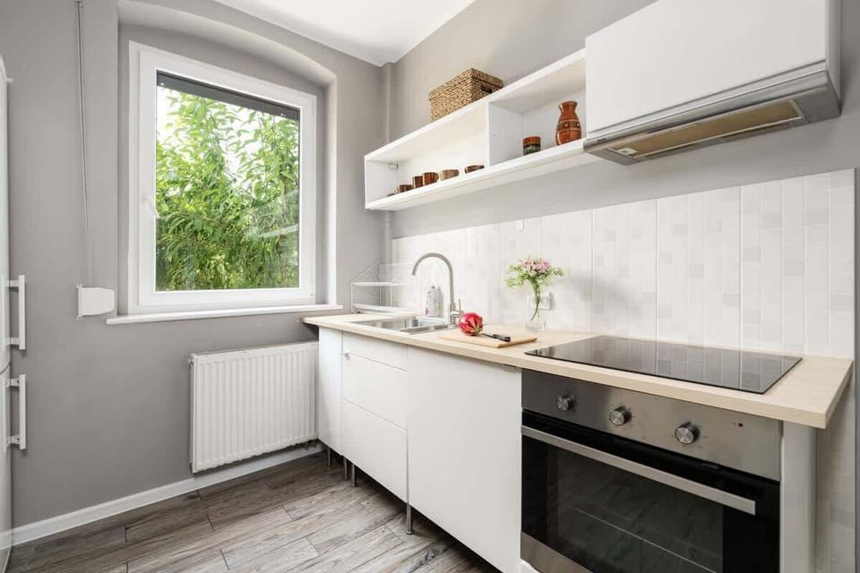 A modern kitchen with sleek white cabinetry, a built-in oven, and a large window overlooking greenery.

