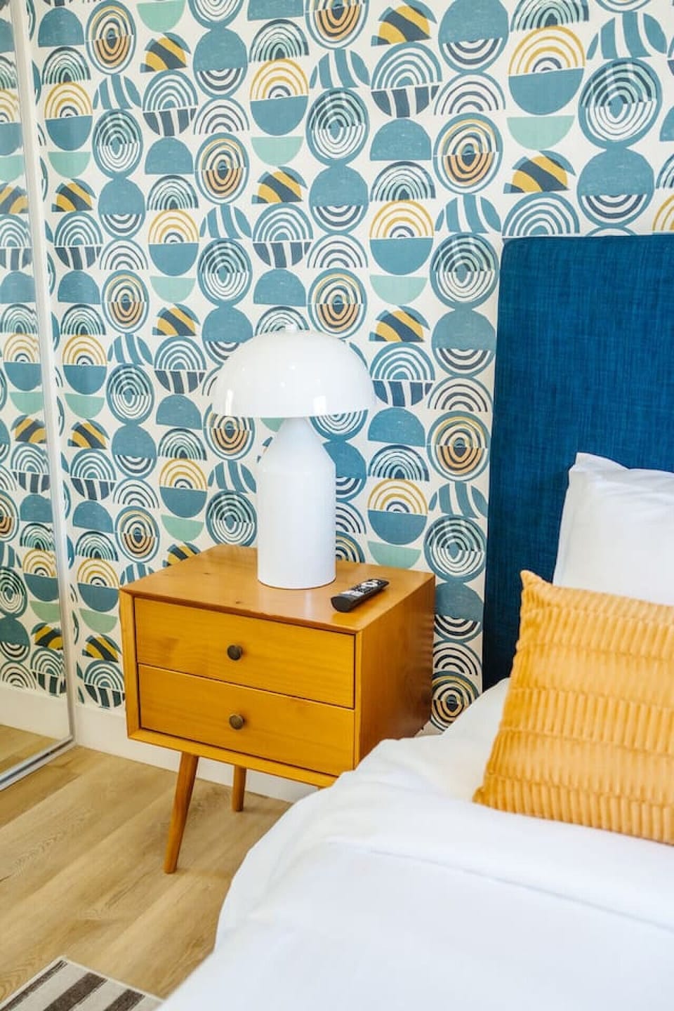 Bedside vignette w/ patterned wallpaper, sculptural lamp & warm wood nightstand.