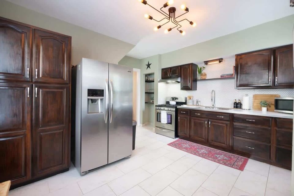 Cook in style with sleek appliances, rich wood cabinets, and open shelving. Thoughtful details like glassware, cookbooks, and a cozy rug add character to this bright, welcoming space! 