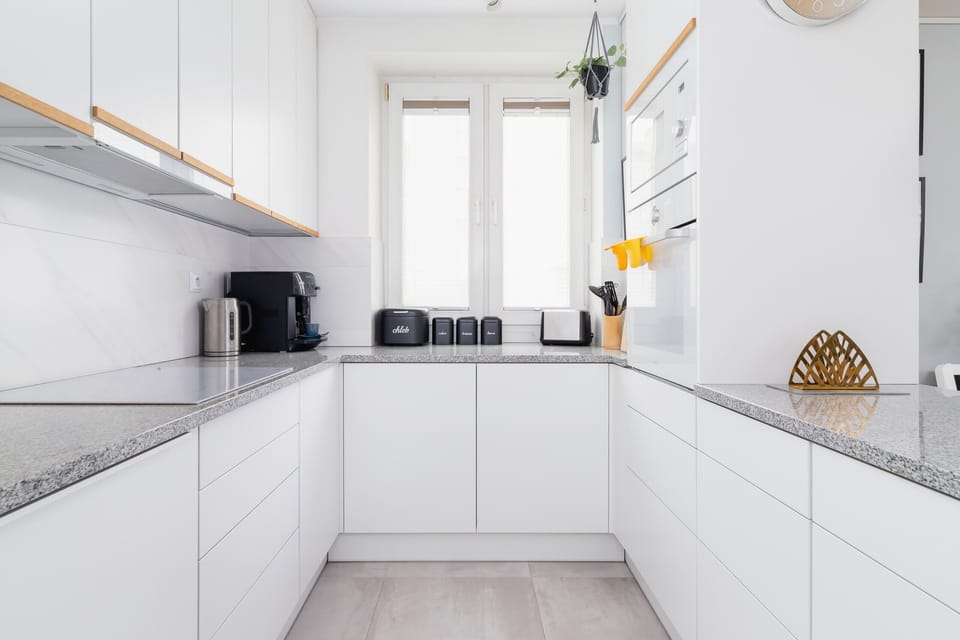A modern kitchen with sleek white cabinetry, marble countertops, and ample natural light.

