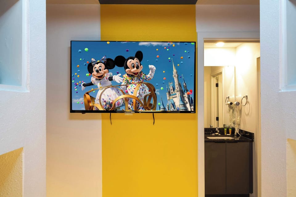 Mickey & Minnie-themed TV nook with a cheerful yellow accent wall; an en-suite vanity nearby makes movie nights and quick refreshes a breeze!