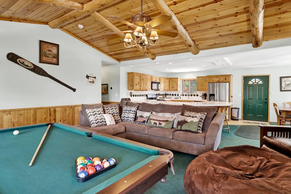 Cozy mountain living room with a stone fireplace, comfy seating, smart TV, and a nearby pool table—perfect for relaxing evenings, movie nights, and fun after outdoor adventures.