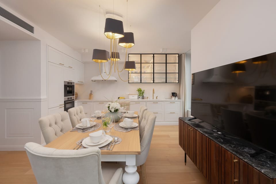 A luxurious dining area with a large table, modern lighting, and natural light streaming through windows.

