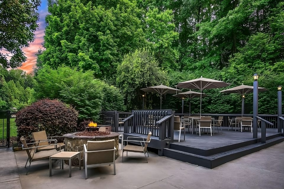Unwind fireside under umbrellas and tall trees at dusk.