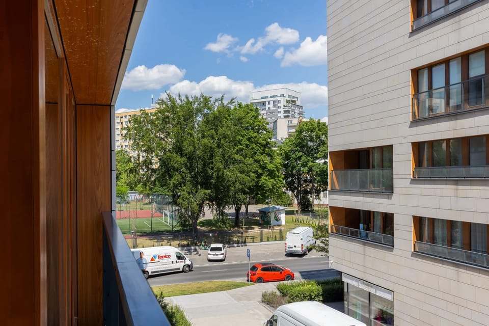 Outdoor view of a residential area with a landscaped garden, parked cars, and vibrant greenery.
