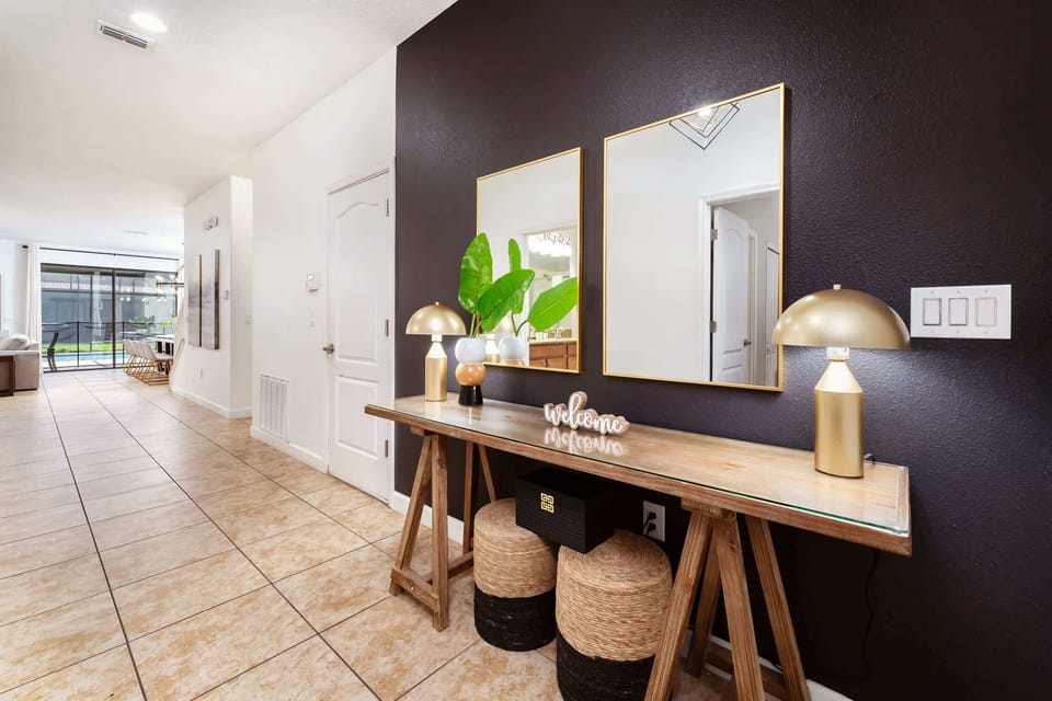 Private entry foyer with gold-framed mirrors, tropical greenery, and a welcoming view toward the screened pool area.
