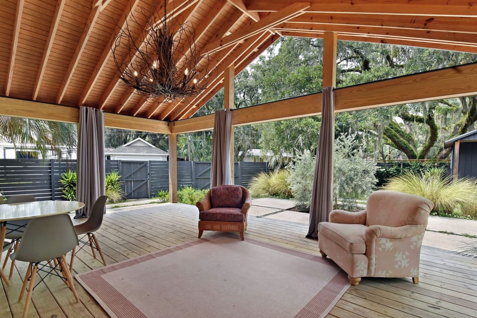 Covered Patio and Fenced Yard - Vaulted covered patio with lounge seating, ceiling fan, chandelier, curtains, and view into the fenced yard.