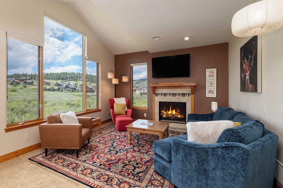 Unwind by your crackling fireplace with sweeping mountain views through floor-to-ceiling windows in this cozy living space.