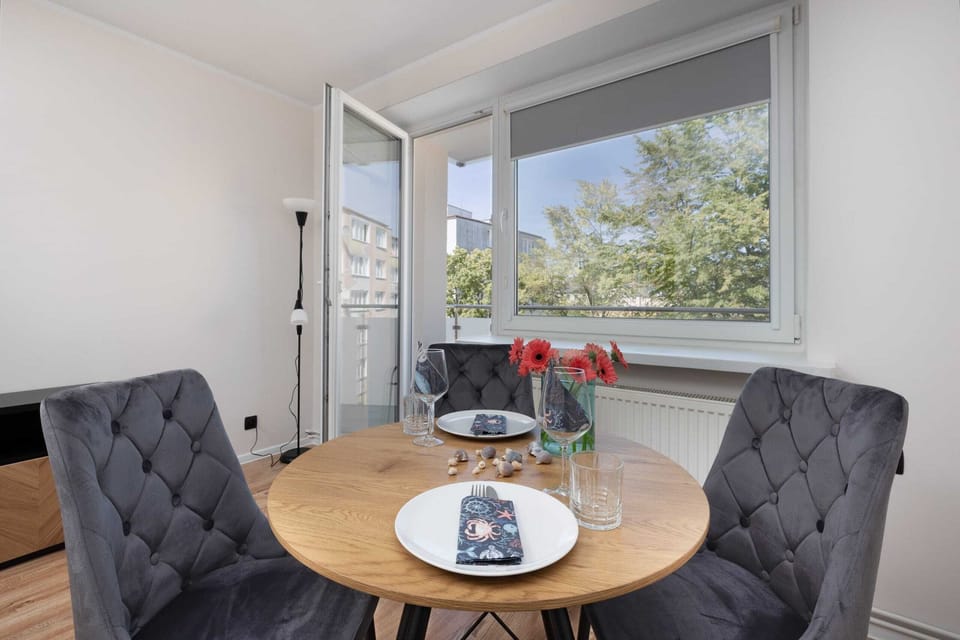 Dining area with a round wooden table and elegant grey chairs, complemented by natural light.

