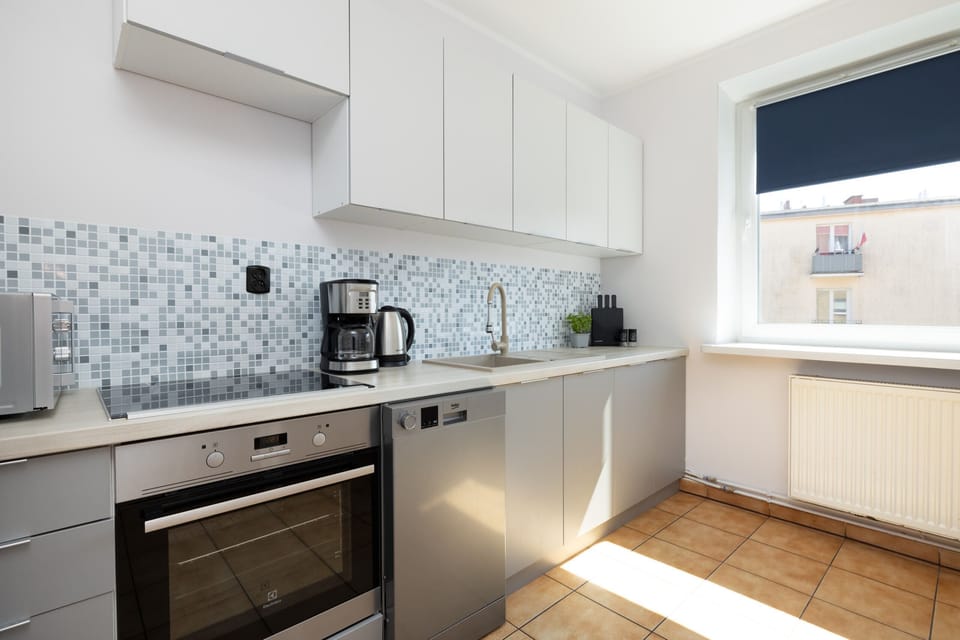 Modern kitchen with white cabinets, tiled backsplash, and stainless steel appliances.

