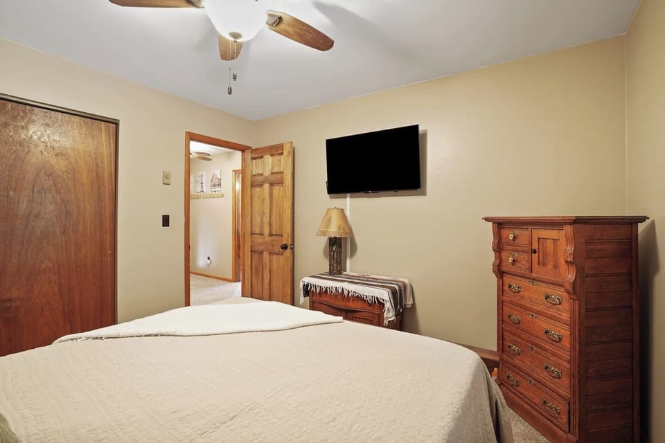Unwind in this cozy bedroom featuring a comfortable bed with soft linens, warm wood furnishings, and a flat-screen TV, perfect for relaxing after a day of adventure before drifting into a peaceful night’s sleep.