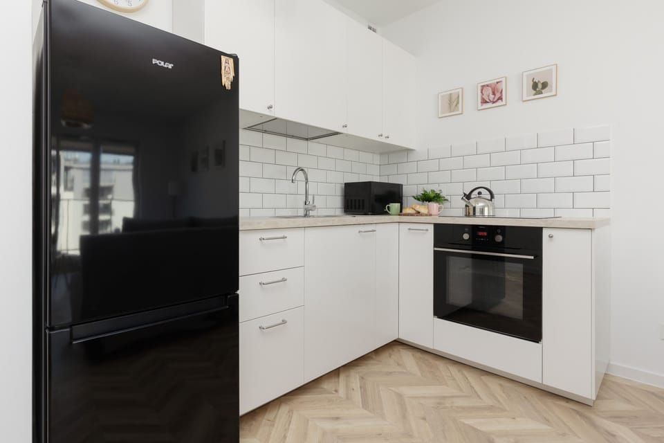 A kitchen corner featuring white cabinets, a black refrigerator, and a tiled backsplash.

