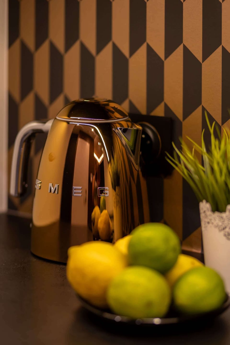 A kitchen counter close-up with a kettle, fresh fruit, and a bold geometric backsplash.


