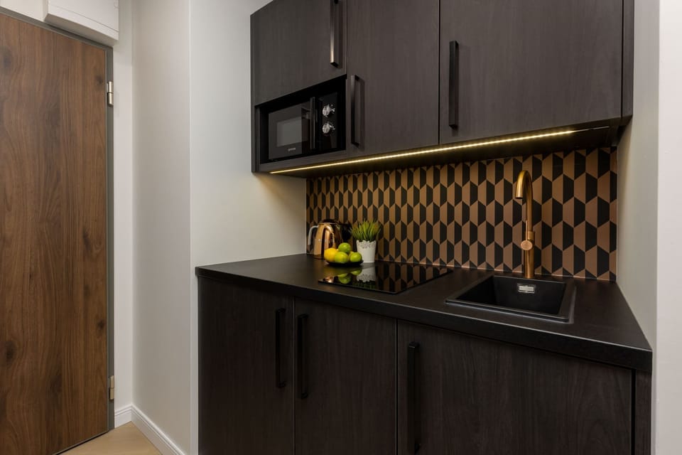 A compact kitchenette with dark cabinets, a geometric backsplash, and convenient appliances.


