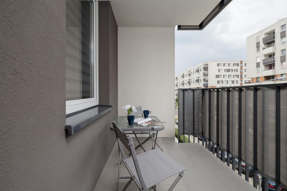 A balcony with a small table and chairs, providing a cozy outdoor spot with a view of the residential area.

