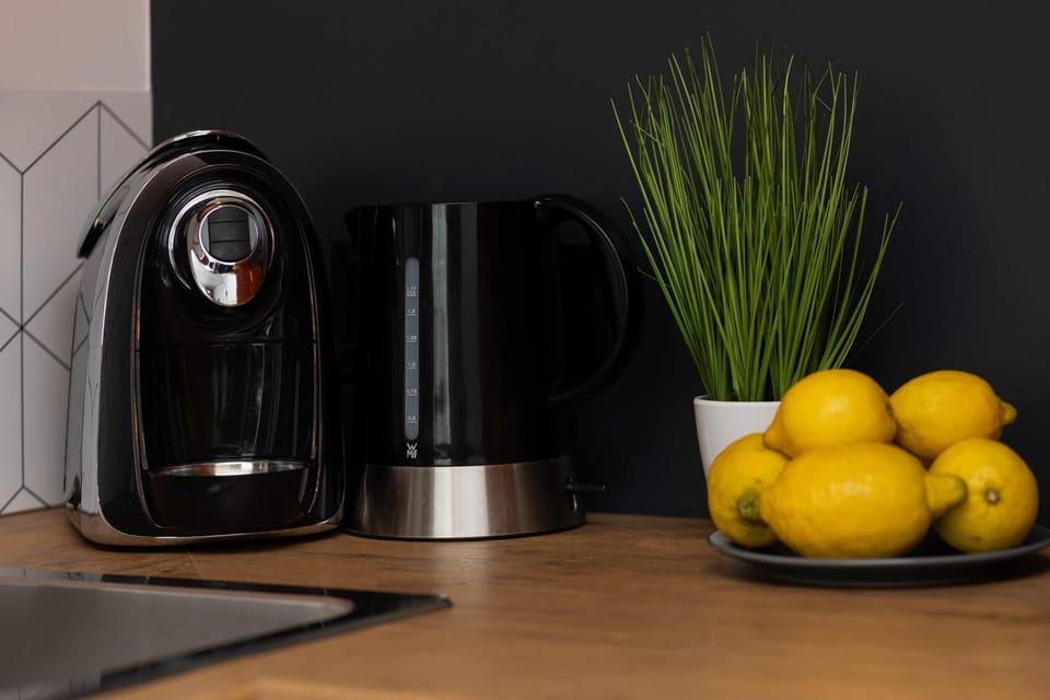 A close-up of a kitchen corner with a kettle, coffee maker, and fresh lemons adding a homey vibe.

