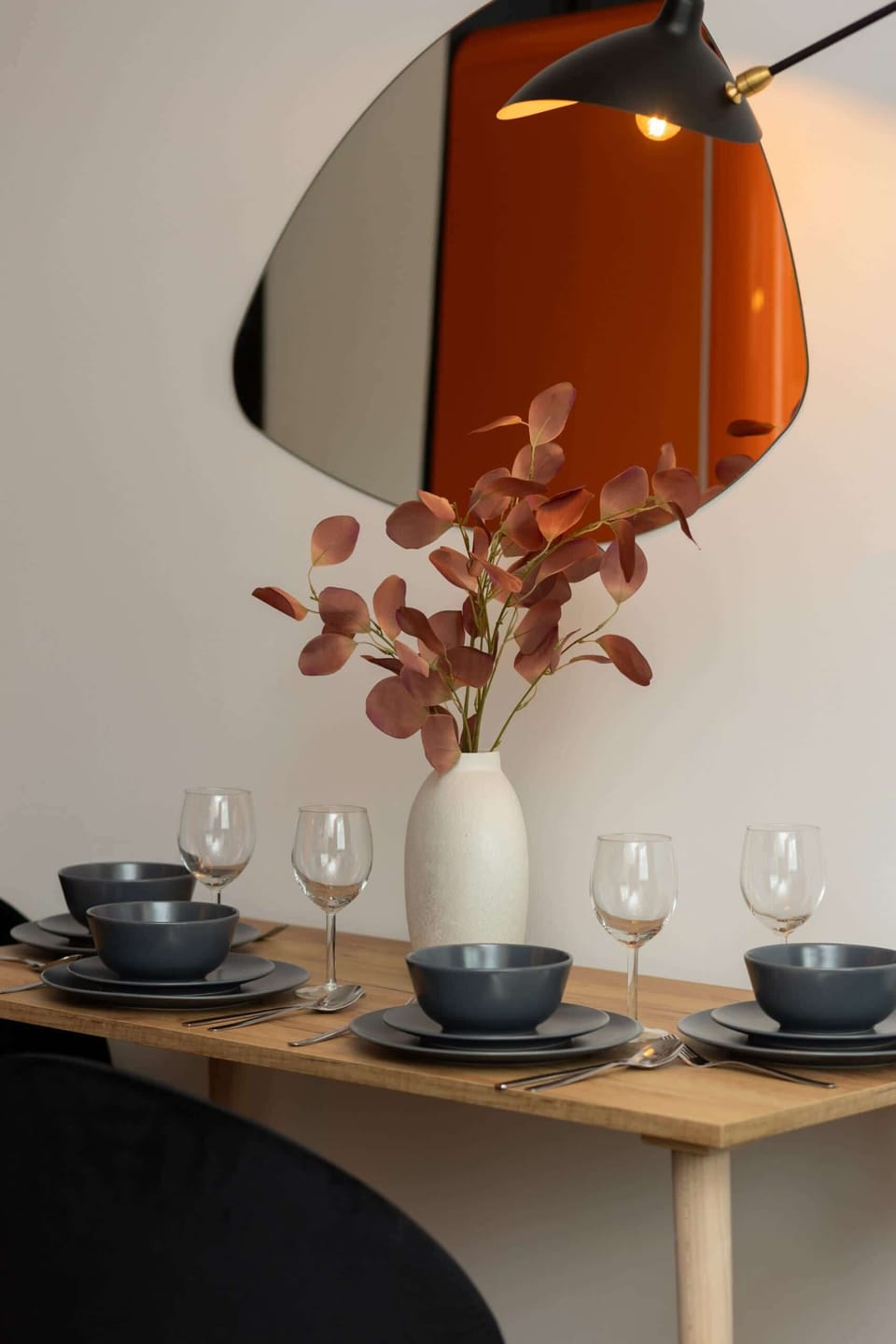 A close-up of a dining table set with elegant tableware and an orange pendant lamp overhead.

