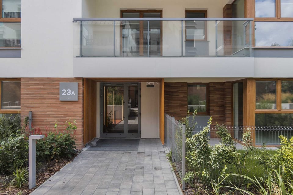 An exterior view of the building’s entrance, with glass balconies and a landscaped walkway.

