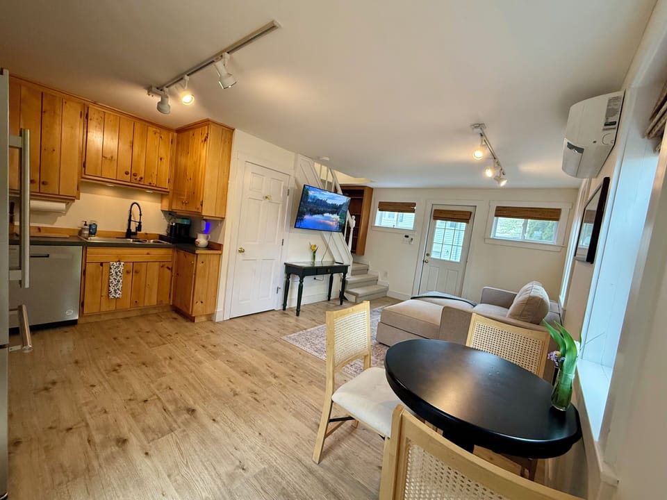 Room 8's lower level features a fully equipped kitchen with wood cabinetry, a dining table for two, and a cozy lounge area with a sectional and smart TV. Perfect for guests seeking space, functionality, and comfort during their coastal Maine stay.
